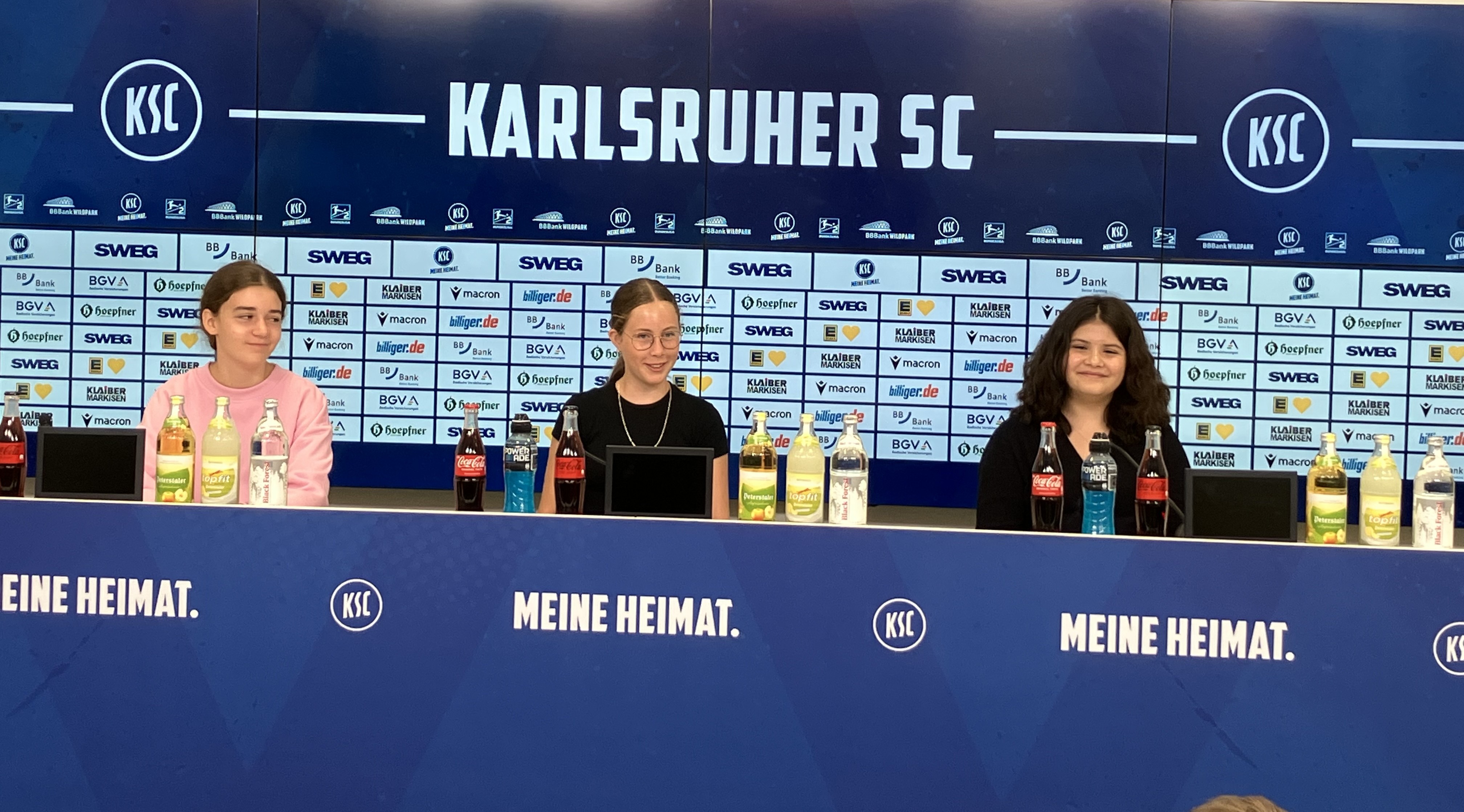 03 Drei Schülerinnen sitzen auf den Sprecherplätzen im Presseraum und blicken in die Kamera.